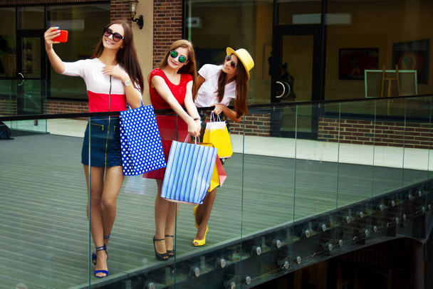 Melko onnellinen kirkas naiset naispuoliset tytöt ystäviä värikkäitä mekkoja, hattuja ja korkokengät ostoskassit tekee selfie ostamisen jälkeen ostoskeskuksessa kesällä. Kauppojen myynti, musta perjantai
. - Valokuva, kuva