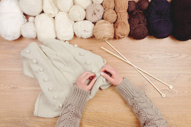 Schneiderarbeitsplatz. Frau weibliches Mädchen Hände Stricken warmen Pullover von gestrickten Nadeln auf hölzernem Hintergrund mit einer Reihe von Fadenbällen - Foto, Bild