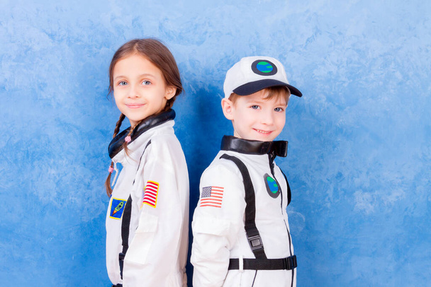 Młody chłopiec i dziewczynka bawią się w astronautę w białym kostiumie astronauty i marzą o lataniu w kosmos na niebieskim tle - Zdjęcie, obraz