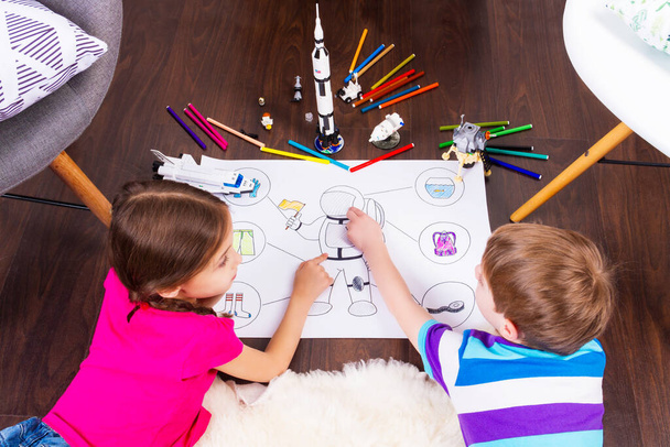 Kleine Kinder malen Astronautenkostüme mit Kugelschreibern und träumen mit Kosmonautenspielzeug vom Kosmos: Rakete, Shuttle und Rover im komfortablen Interieur zu Hause auf Holzboden - Foto, Bild