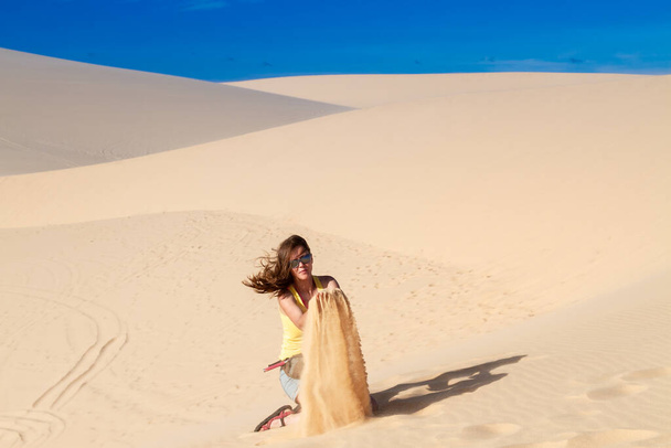 女は砂の上の砂漠に座って指を通して砂を抱いている - 写真・画像
