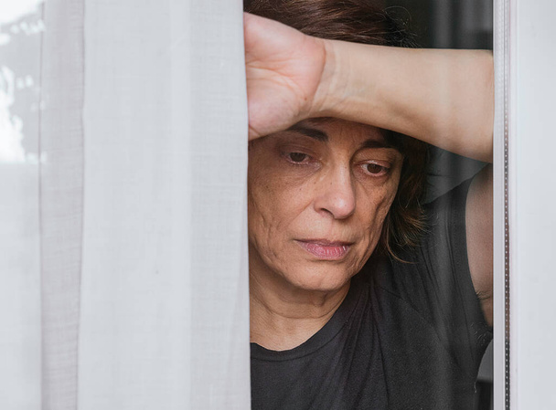  Karantina altındayken endişeli bir kadın pencereden dışarı bakıyor ve dışarı çıkamıyor. - Fotoğraf, Görsel