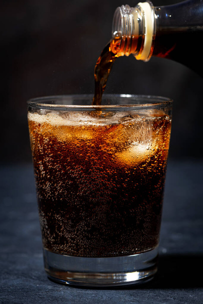 Coca cola is poured into a glass from bottle, closeup - Foto, Imagem