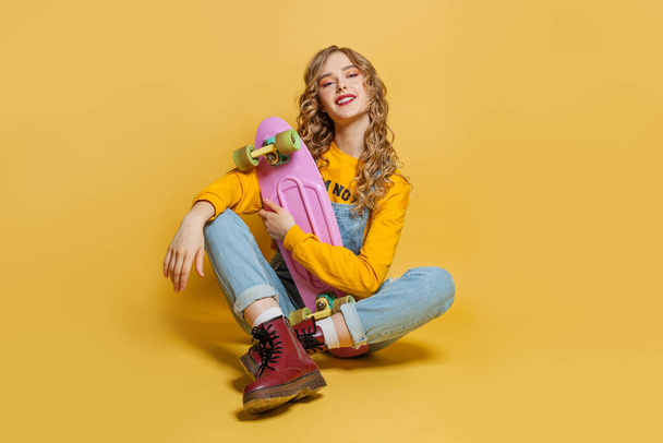 Jeune femme heureuse avec skateboard sur fond jaune vif
 - Photo, image