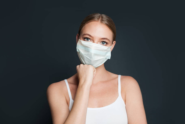 Hübsche Frau mit medizinischer Gesichtsmaske auf schwarzem Hintergrund - Foto, Bild
