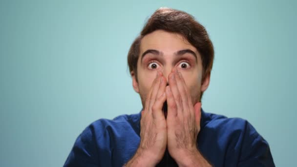 Geschockter Mann bedeckt Mund mit Händen. Mann mit offenem Mund auf blauem Hintergrund - Filmmaterial, Video