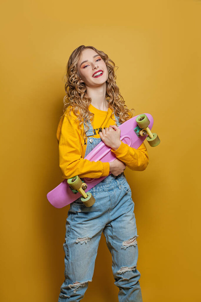 Excited woman with skateboard on bright yellow background. Positive emotion - Foto, imagen