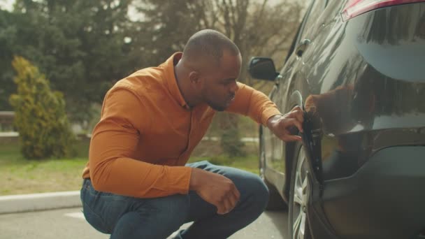 Frustrated african man looking at damaged scratched car - Materiał filmowy, wideo
