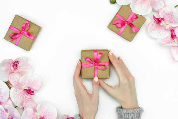 flatlay of Gift present boxes with female hands and pink ribbon with orchid flowers on white background top view. Gift or present spring concept. Copy space - Zdjęcie, obraz