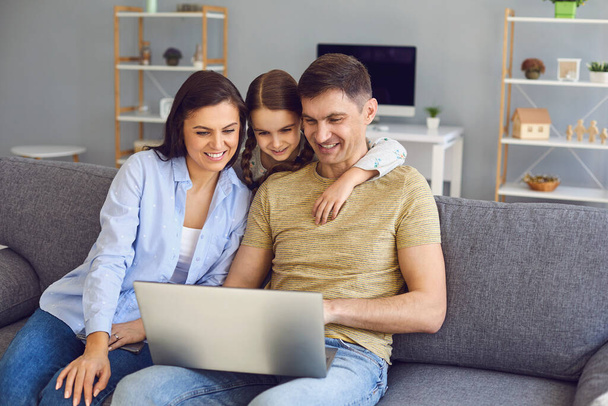 Happy family looking at a laptop while sitting comfortably on a sofa in a living room at the weekend. - Fotoğraf, Görsel