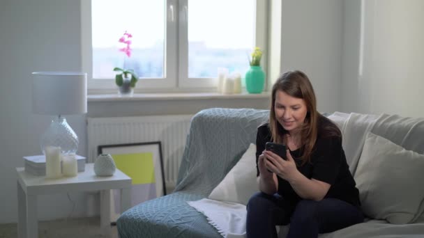Young woman with smartphone at sofa at home. Telephone gadget device - Filmagem, Vídeo