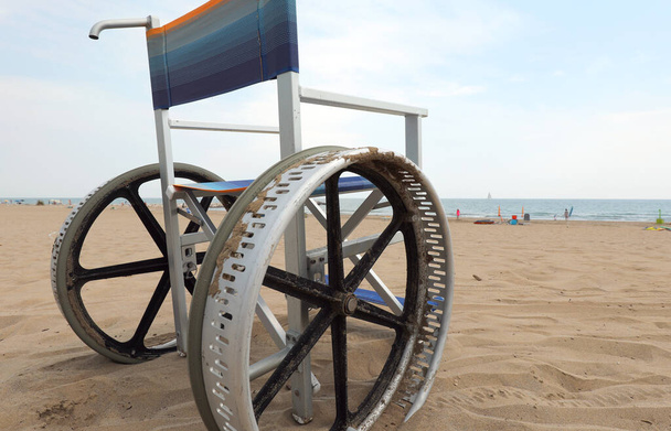 Спеціальний інвалідний візок з великими металевими колесами, щоб легко пересуватися на піщаному пляжі біля моря
 - Фото, зображення