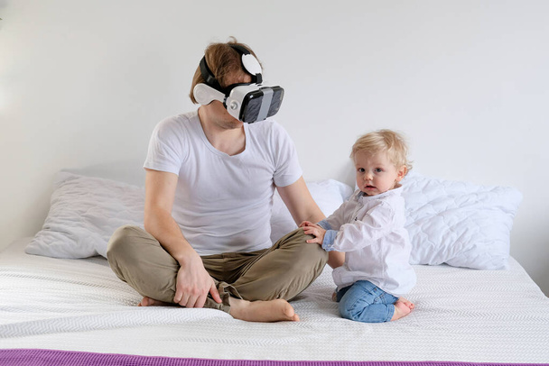 sedící doma, mladý muž hrající si v brýlích vertikální reality. Otec a syn na posteli. Táta si nevšímá dítěte, když hraje počítačové hry. Péče - Fotografie, Obrázek