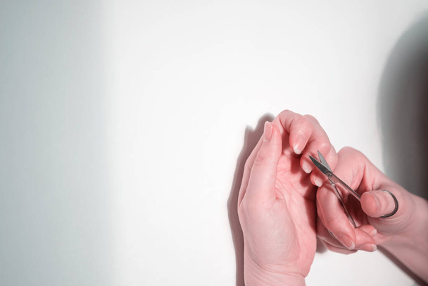 Hands on a white background cut their nails with scissors. Unrecognizable person - Foto, imagen