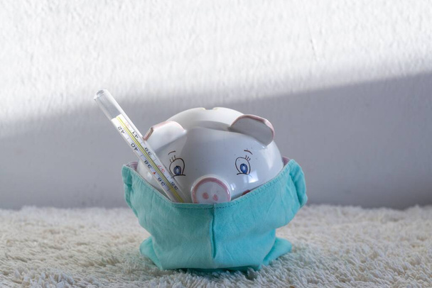 Piggy bank com o termômetro em máscara de respirador apresentando os problemas econômicos e economia financeira durante a pandemia. Eslováquia
 - Foto, Imagem