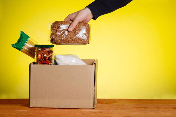 Wolontariusz z pudełkiem darowizn ze środkami spożywczymi na żółtym tle - Zdjęcie, obraz
