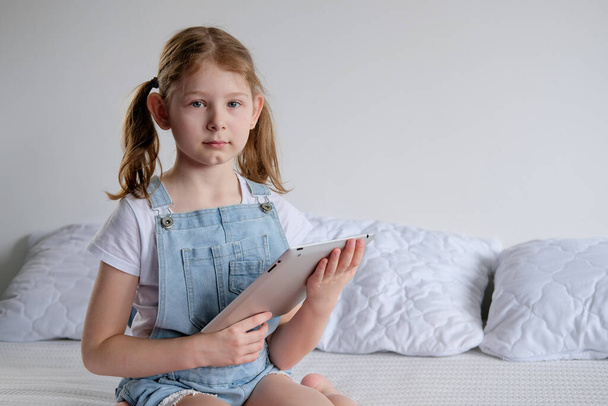 the girl is sitting at home on the bed, and in her hands is a laptop. a schoolgirl learns and plays games on a laptop. Quarantine self-education - Photo, Image