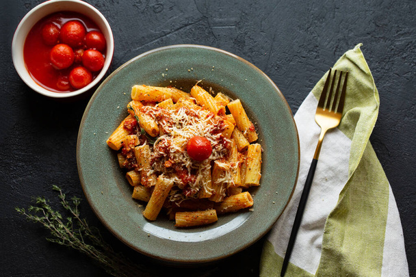 Tasty appetizing classic Italian pasta with tomato sauce, parmesan cheese and noodles on a plate on a dark table.Top view, horizontal.Italian pasta.Penne pasta in tomato sauce with chicken, tomatoes. - Photo, Image
