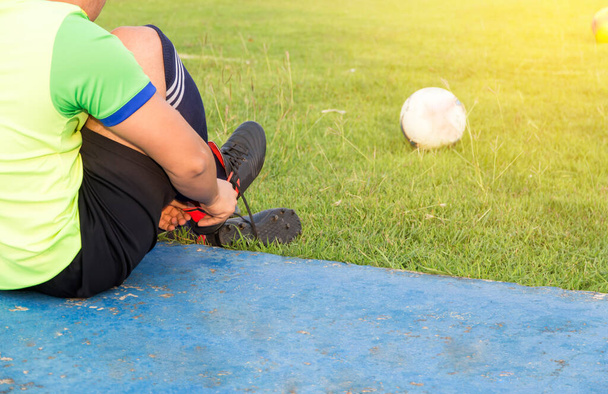 Młody azjatycki sportowiec wiążący buty piłkarskie obok boiska, piłka nożna męska gotowa do gry na boisku, wellness i sport koncepcja - Zdjęcie, obraz