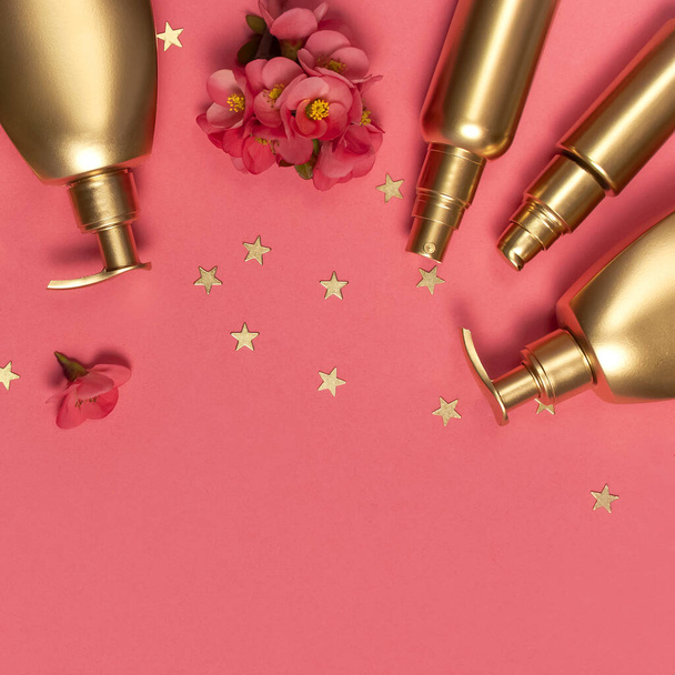 化粧品ブランドのコンセプト。化粧品、春のピンクの花、ピンクの背景に金の星のコンフェッティ。化粧品のモックアップゴールドボトル。フラットレイアウトトップビューコピースペース。化粧品、美容の背景. - 写真・画像