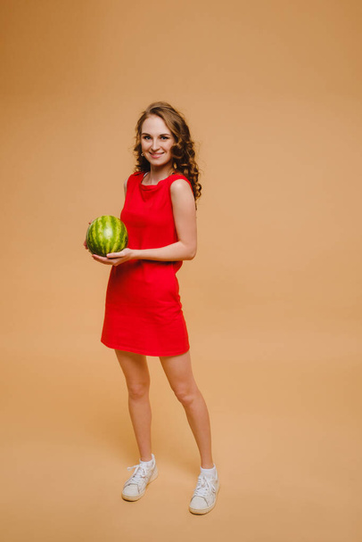 A beautiful girl in glasses and a red dress holds a watermelon in her hands. - Fotó, kép