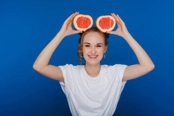 Surprised, the laughing girl holds the grapefruit like ears. Vegan lifestyle. Smiling woman , eating concept.Diet organic , weight loss and healthy food. Smoothies and fresh juice - 写真・画像