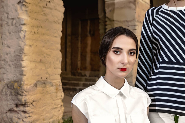 Outdoor fashion portrait of two young beautiful women wearing fashionable clothes posing on the street against the background of an old abandoned building. - Foto, imagen