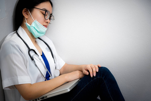 アジアの若い女性医師は安全のためにマスクを着用コロナウイルスは、過労の概念から疲労で寝て角床に座って自分自身をケアすることは、医師が流行を停止するのを助けることですCovid-19ウイルス - 写真・画像
