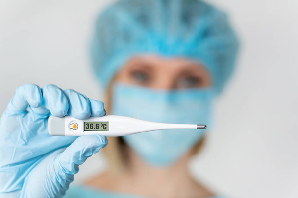 女性医師または看護師は温度を測定するための電子温度計を保持します。温度計に焦点を当てたフィールドの深さ - 写真・画像