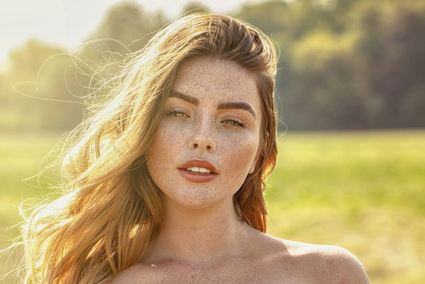 Nature, summer holidays, vacation. Happy young woman enjoying sun on countryside. Closeup beauty portrait of redhead girl with freckles. - Foto, afbeelding