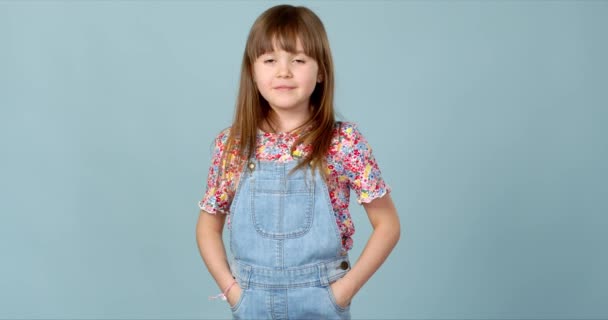 Linda niña de pie en jeans dungarees con las manos en los bolsillos
 - Imágenes, Vídeo