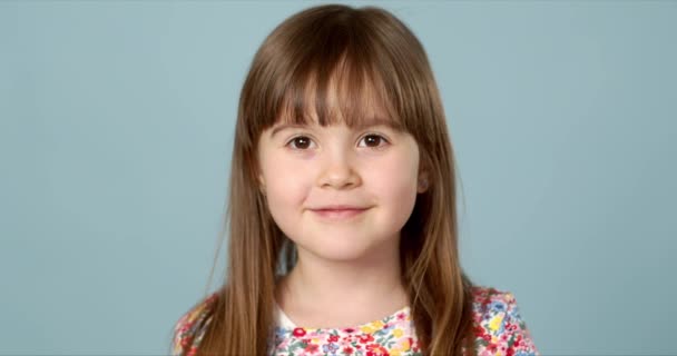 Potrait of nice smiling little girl with logng hair posing over blue background in studio - Imágenes, Vídeo