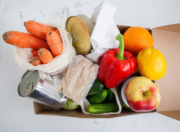 Box with products for donation. Canned food, cereals, fruits, vegetables. White background, top view. - 写真・画像