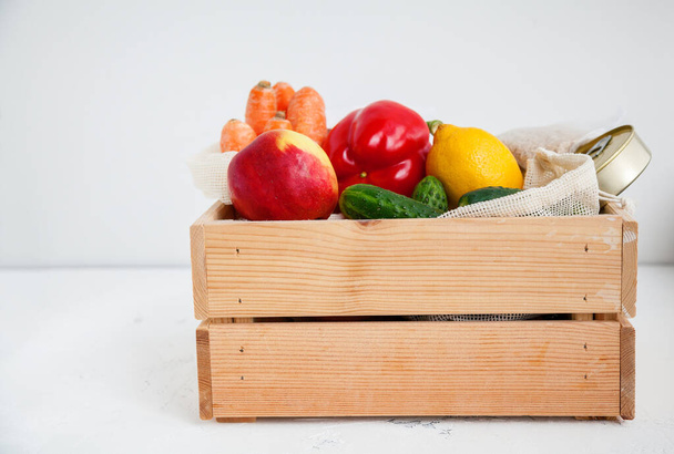 Donation wooden box with various food. Canned food, cereals, fruits, vegetables. White background, copy-space. - Fotó, kép