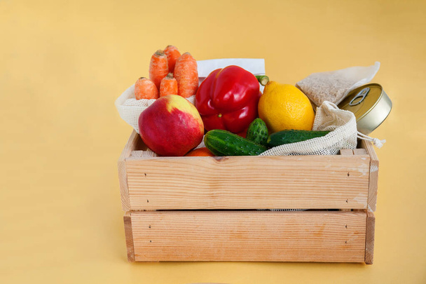 Donation wooden box with various food. Canned food, cereals, fruits, vegetables. Yellow background, copy-space. - Φωτογραφία, εικόνα