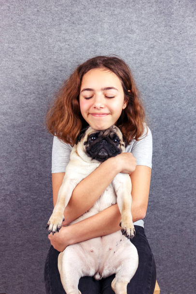 Тварини люблять. Кучерява дівчина-підліток обіймає свого сумного мопса собаку
 - Фото, зображення