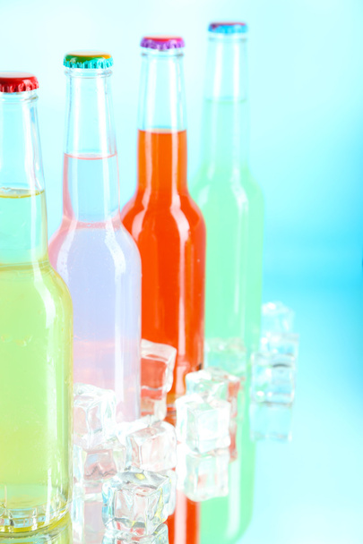 Drinks in glass bottles with ice cubes on blue background - Foto, imagen