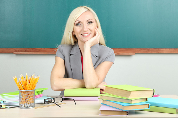 School teacher sitting at table on blackboard background - Photo, Image