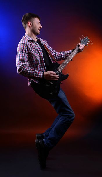 Young musician playing guitar on dark color background - Foto, immagini