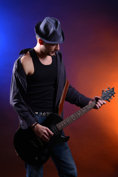 Young musician playing guitar on dark color background - Foto, Imagen