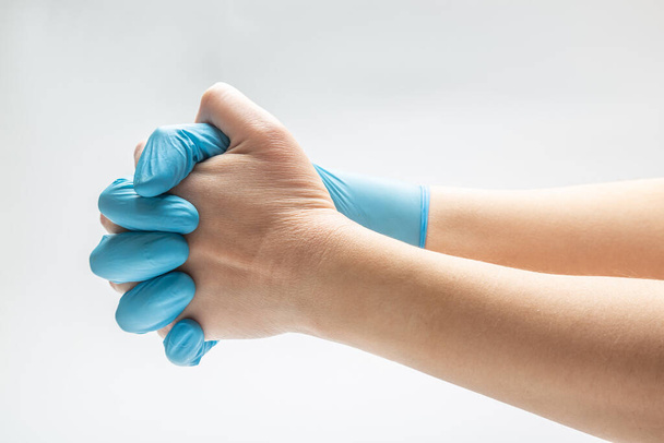 mano sostiene una mano en un guante médico azul sobre un fondo blanco. dedos cruzados de manos. oración. Orientación horizontal. Alta calidad
 - Foto, imagen