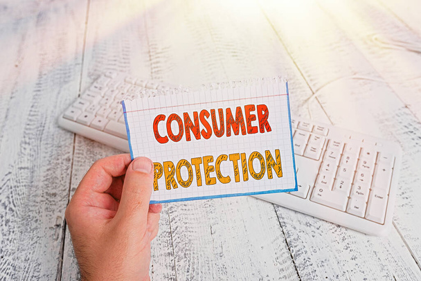 Σήμα κειμένου που δείχνει την προστασία των καταναλωτών. Έννοια φωτογραφία Δίκαιο Εμπόριο Νόμοι για να εξασφαλίσει την προστασία των καταναλωτών άνθρωπος κρατώντας πολύχρωμο υπενθύμιση τετράγωνο σχήμα χαρτί λευκό πληκτρολόγιο ξύλινο πάτωμα. - Φωτογραφία, εικόνα