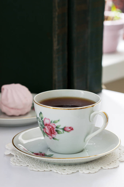 Tea in a vintage cup, marshmallows on a vintage saucer and old books on a light background. Selective focus. - Zdjęcie, obraz