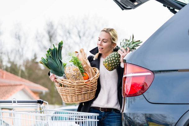 Frau lädt Lebensmittel nach Einkauf in Kofferraum ihres Autos - Foto, Bild