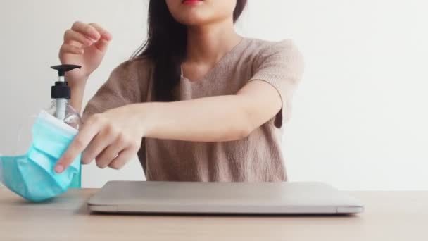 Mujer asiática usando gel de alcohol mano desinfectante lavar la mano antes de abrir el ordenador portátil para proteger coronavirus. Las mujeres empujan el alcohol para limpiar la higiene cuando el distanciamiento social permanece en casa y el tiempo de auto cuarentena - Imágenes, Vídeo