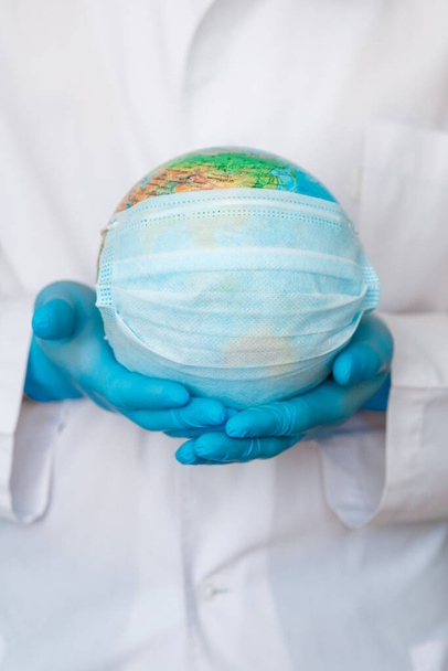 globe with a medical mask from covid-19 virus in hands ofdoctor close-up. concept epidemic and pandemic of Coronavirus. - Фото, зображення