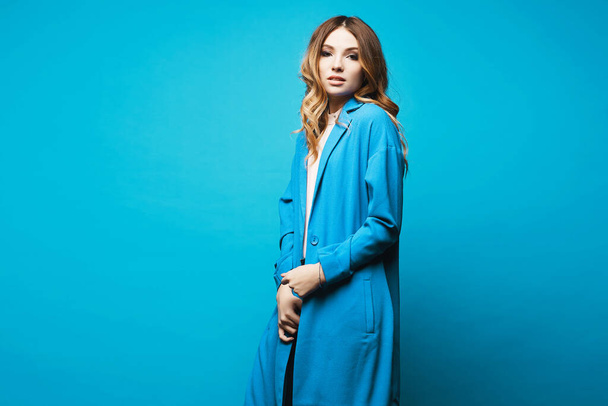 Young woman with tender makeup and in trendy blue coat posing over blue background, isolated. Copy space. Female fashion. - Photo, image