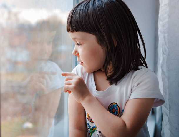 una bambina a casa durante la quarantena guarda attraverso il vetro della finestra, si spera. Autoisolamento dalla pandemia mondiale di Covid-19 coronavirus
 - Foto, immagini