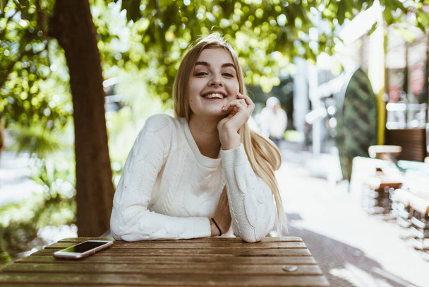 joyful beautiful blonde smiles amiably sitting at a table of a street cafe - 写真・画像