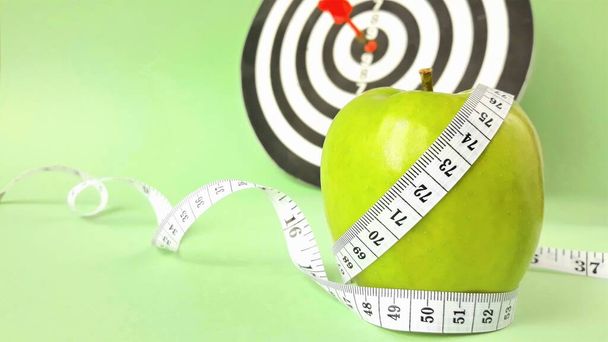 Fresh green fruits wrapped in a measuring tape on a dart background.Concept of the goal to lose weight, the goal of diet
 - Фото, изображение